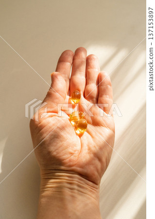 Close-up of woman's hand holding capsules with nutritional supplements, warm sunlight. A healthy lifestyle, daily vitamin intake preventative medicine Close-up of woman's hand holding capsules with nutritional supplements, warm sunlight. A healthy lifestyle, daily vitamin intake preventative medicine 137153897