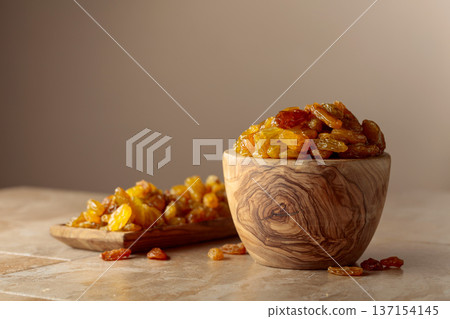 Yellow sultana raisins in a wooden bowl on a beige background. Yellow sultana raisins in a wooden bowl on a beige background. 137154145