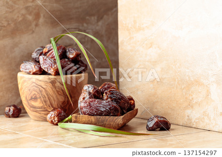 Dates fruit in a wooden dish on a beige ceramic table. 137154297