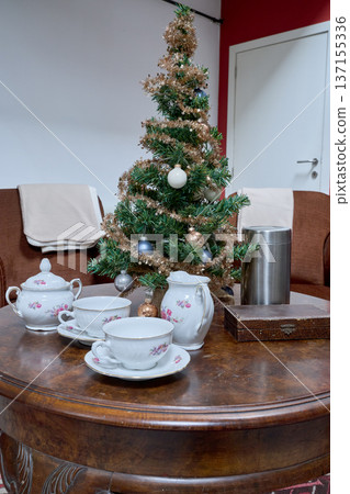 Artificial Christmas tree placed on a round living room table with a tea set 137155336