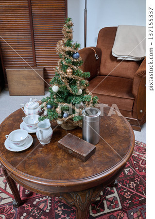 Artificial Christmas tree placed on a round living room table with a tea set 137155337