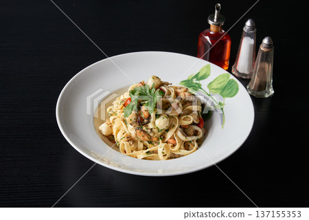 Plate of tagliatelle pasta with seafood on a black wooden table Plate of tagliatelle pasta with seafood on a black wooden table 137155353