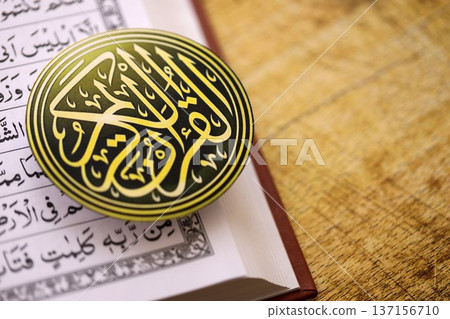 Sign with Al Quran inscription on Muslim holy book in mosque. Details of arabic calligraphy on sticker. Concept of Islam religion and praying in arabic countries Sign with Al Quran inscription on Muslim holy book in mosque. Details of arabic calligraphy on sticker. Concept of Islam religion and praying in arabic countries 137156710
