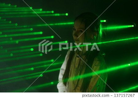 A girl in the green rays of a maze laser in a black room A girl in the green rays of a maze laser in a black room 137157267
