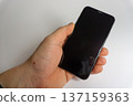 Hand holding a smartphone with black screen in home environment during daytime 137159363