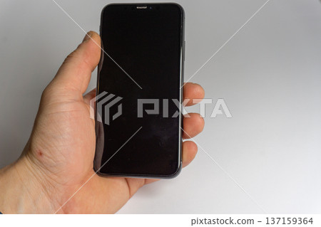 Hand holds a smartphone with a dark screen in a plain white setting during daytime Hand holds a smartphone with a dark screen in a plain white setting during daytime 137159364