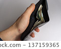 Person holds a black wallet with cash inside in a well lit indoor setting during daylight hours 137159365