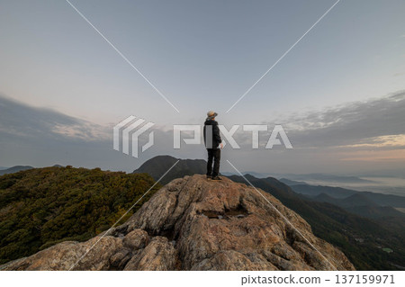 The back view of a climber standing on the summit and the pre-dawn sky The back view of a climber standing on the summit and the pre-dawn sky 137159971