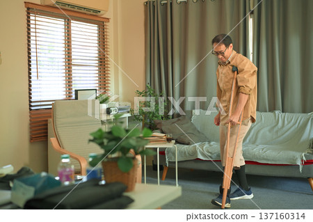 Middle aged man walking at home with a prosthetic leg and crutches Middle aged man walking at home with a prosthetic leg and crutches 137160314