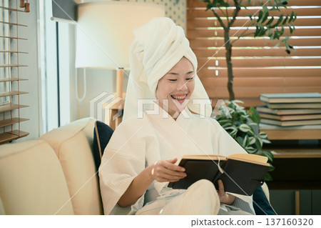 Young woman in bathrobe reads book on sofa Young woman in bathrobe reads book on sofa 137160320