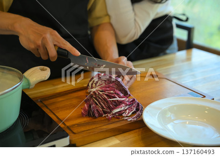 Cropped shot couple cooking together at home, slicing fresh red cabbage on a wooden board 137160493