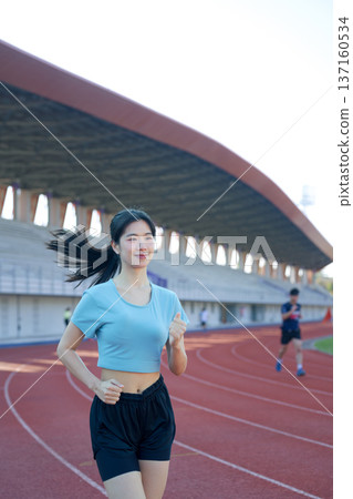 Young Asian woman jogging on outdoor running track at stadium, morning exercise 137160534
