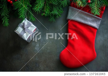 Christmas stocking and gift wrapped in silver surrounded by pine branches on a stone surface Christmas stocking and gift wrapped in silver surrounded by pine branches on a stone surface 137161043