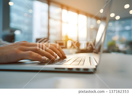 Close up of hands typing on a laptop keyboard with a blurred background of a modern office 137162353