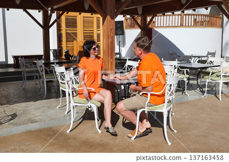 An adult man and woman in summer clothes are talking while sitting at a cafe table An adult man and woman in summer clothes are talking while sitting at a cafe table 137163458