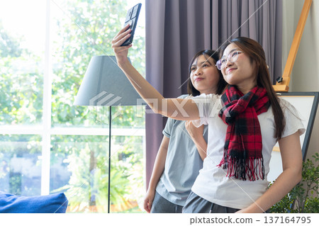 Capturing the Moment: Friends taking selfie indoors. A vibrant capture of two cheerful friends joyfully taking a selfie together indoors, capturing the essence of modern friendship, framed by a soft. 137164795