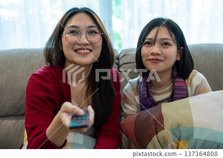 Cozy Relaxation: Two companions find comfort together on the couch, smiling while watching TV, enjoying a tranquil moment of shared leisure. Cozy Relaxation: Two companions find comfort together on the couch, smiling while watching TV, enjoying a tranquil moment of shared leisure. 137164808