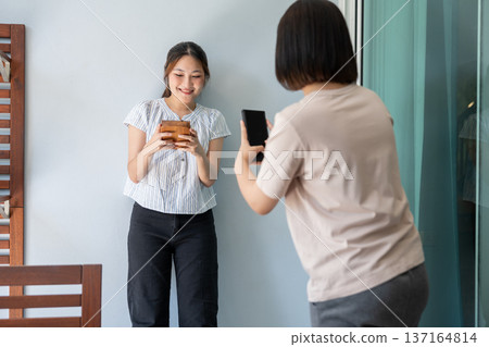Capturing the Moment: A candid scene of friendship unfolds as one person captures a photograph of a happy individual holding an object. It's a sweet moment of connection and joy. Capturing the Moment: A candid scene of friendship unfolds as one person captures a photograph of a happy individual holding an object. It's a sweet moment of connection and joy. 137164814
