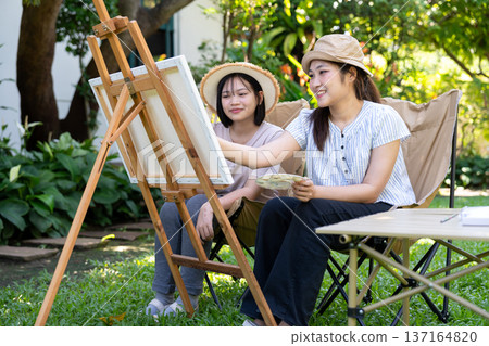 Artistic Companionship: Two friends share a creative moment, painting together outdoors under a serene, sun-drenched sky. Artistic Companionship: Two friends share a creative moment, painting together outdoors under a serene, sun-drenched sky. 137164820
