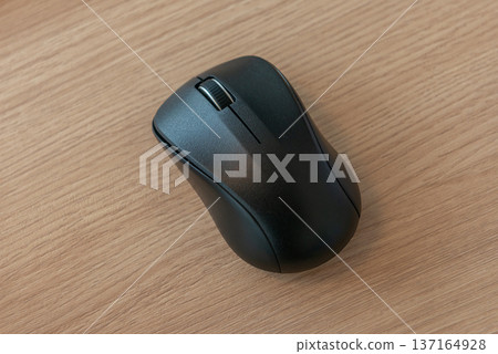 A black wireless mouse on a wooden desk 137164928