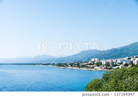 Clear blue sea and buildings lining the coastline under bright sunlight on the French island of Corsica in the Mediterranean Sea 137164947