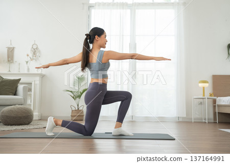 Young Asian woman in sportswear doing yoga in her home or house for health, sports and wellness, Enjoying Domestic Fitness Training And Healthy Lifestyle, Dressed In Stylish Sportswear And Smiling Young Asian woman in sportswear doing yoga in her home or house for health, sports and wellness, Enjoying Domestic Fitness Training And Healthy Lifestyle, Dressed In Stylish Sportswear And Smiling 137164991