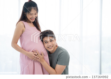 A loving husband gently kisses, listens to the sound of his unborn and gently caressing his pregnant wife belly, a tender moment of anticipation and connection, filled with joy of expecting a child. 137164992