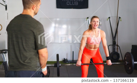 Woman lifting barbell with trainer in gym Woman lifting barbell with trainer in gym 137166119