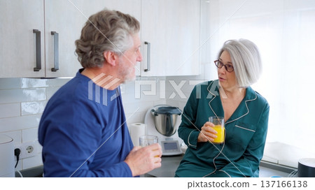 Senior couple sharing morning conversation in kitchen pajamas Senior couple sharing morning conversation in kitchen pajamas 137166138