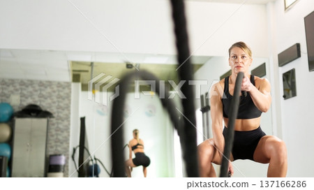 Determined woman training with battle ropes in gym Determined woman training with battle ropes in gym 137166286