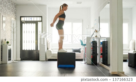 Woman exercising box jumps for strength training workout 137166323