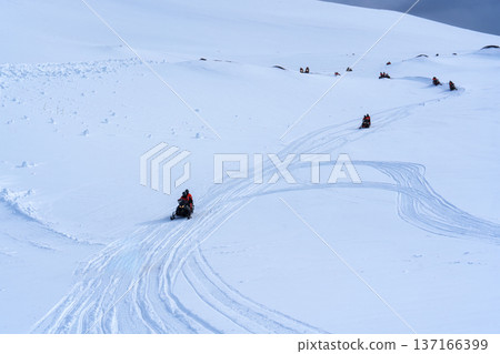 Tourists riding snowmobile on snowy glacier mountain landscape 137166399