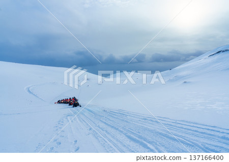 Tourists riding snowmobile on snowy glacier mountain landscape 137166400