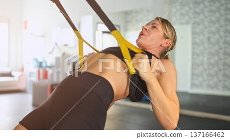 Woman training upper body with suspension straps in gym Woman training upper body with suspension straps in gym 137166462