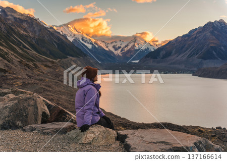 Woman sitting on rock admiring Tasman Lake and snowcapped mountain at sunset in New Zealand Woman sitting on rock admiring Tasman Lake and snowcapped mountain at sunset in New Zealand 137166614