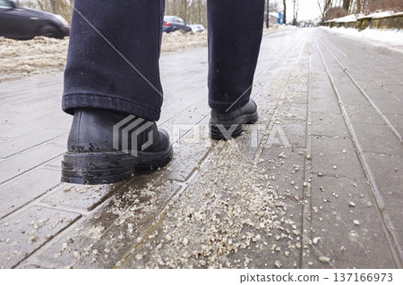Salt on the pavement in the winter, a woman's feet in boots walking 137166973
