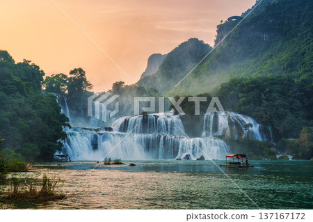 Ban Gioc Waterfall flowing with tourist wooden raft floating to see nearby waterfall in the evening 137167172