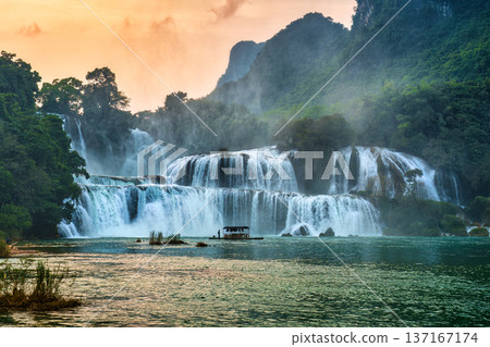 Ban Gioc Waterfall flowing with tourist wooden raft floating to see nearby waterfall in the evening Ban Gioc Waterfall flowing with tourist wooden raft floating to see nearby waterfall in the evening 137167174