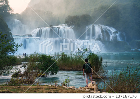 Ban Gioc Waterfall flowing with male tourist standing on the rock 137167176