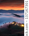 Vibrant sunrise over foggy mountain and illuminated campsite on hill in countryside 137167301