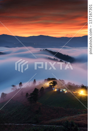 Vibrant sunrise over foggy mountain and illuminated campsite on hill in countryside 137167301