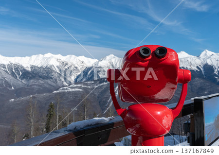 Red panoramic viewer overlooking snowy mountain range in Krasnaya Polyana stands on observation deck against blue winter sky, Travel destination concept for tourism marketing, alpine resort Red panoramic viewer overlooking snowy mountain range in Krasnaya Polyana stands on observation deck against blue winter sky, Travel destination concept for tourism marketing, alpine resort 137167849