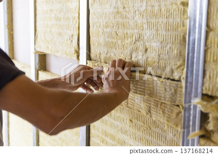Worker insulating a room wall with mineral rock wool thermal insulation. 137168214