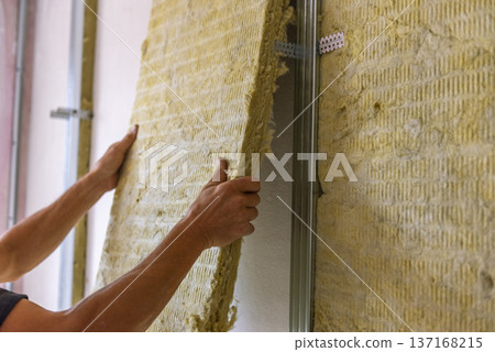 Worker insulating a room wall with mineral rock wool thermal insulation. Worker insulating a room wall with mineral rock wool thermal insulation. 137168215