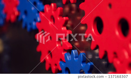 Closeup of colorful gear shapes on a wall, blue cog in sharp focus with red gears blurred behind. Mechanical visuals symbolize teamwork, systems thinking, and smooth collaboration. Closeup of colorful gear shapes on a wall, blue cog in sharp focus with red gears blurred behind. Mechanical visuals symbolize teamwork, systems thinking, and smooth collaboration. 137168307