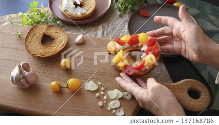 Anonymous person prepares round bruschetta with creamy goat cheese and cherry tomatoes in kitchen. Italian cuisine, high-quality farm-grown ingredients. 137168786
