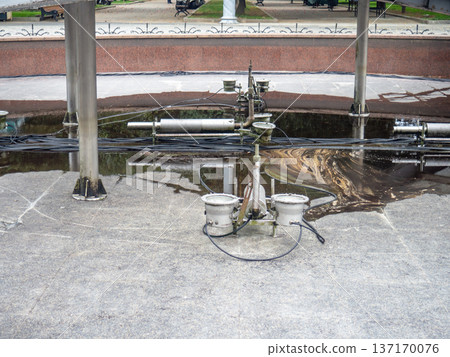 Empty fountain in a city park. Dehumidification. Cleaning the fountain with a hose. The device of the fountain. Pipes for water supply. Water hoses. Modern technologies Empty fountain in a city park. Dehumidification. Cleaning the fountain with a hose. The device of the fountain. Pipes for water supply. Water hoses. Modern technologies 137170076