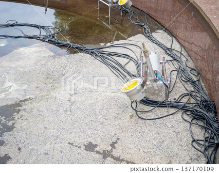 Empty fountain in a city park. Dehumidification. Cleaning the fountain with a hose. The device of the fountain. Pipes for water supply. Water hoses. Modern technologies Empty fountain in a city park. Dehumidification. Cleaning the fountain with a hose. The device of the fountain. Pipes for water supply. Water hoses. Modern technologies 137170109