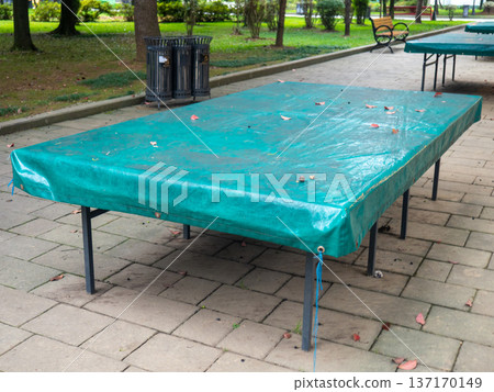 Ping pong tables covered with tarpaulin. Protect mouth from rain. End of summer concept in the park. sport in the park. holiday at the resort Ping pong tables covered with tarpaulin. Protect mouth from rain. End of summer concept in the park. sport in the park. holiday at the resort 137170149