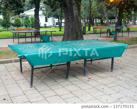Ping pong tables covered with tarpaulin. Protect mouth from rain. End of summer concept in the park. sport in the park. holiday at the resort. 137170155